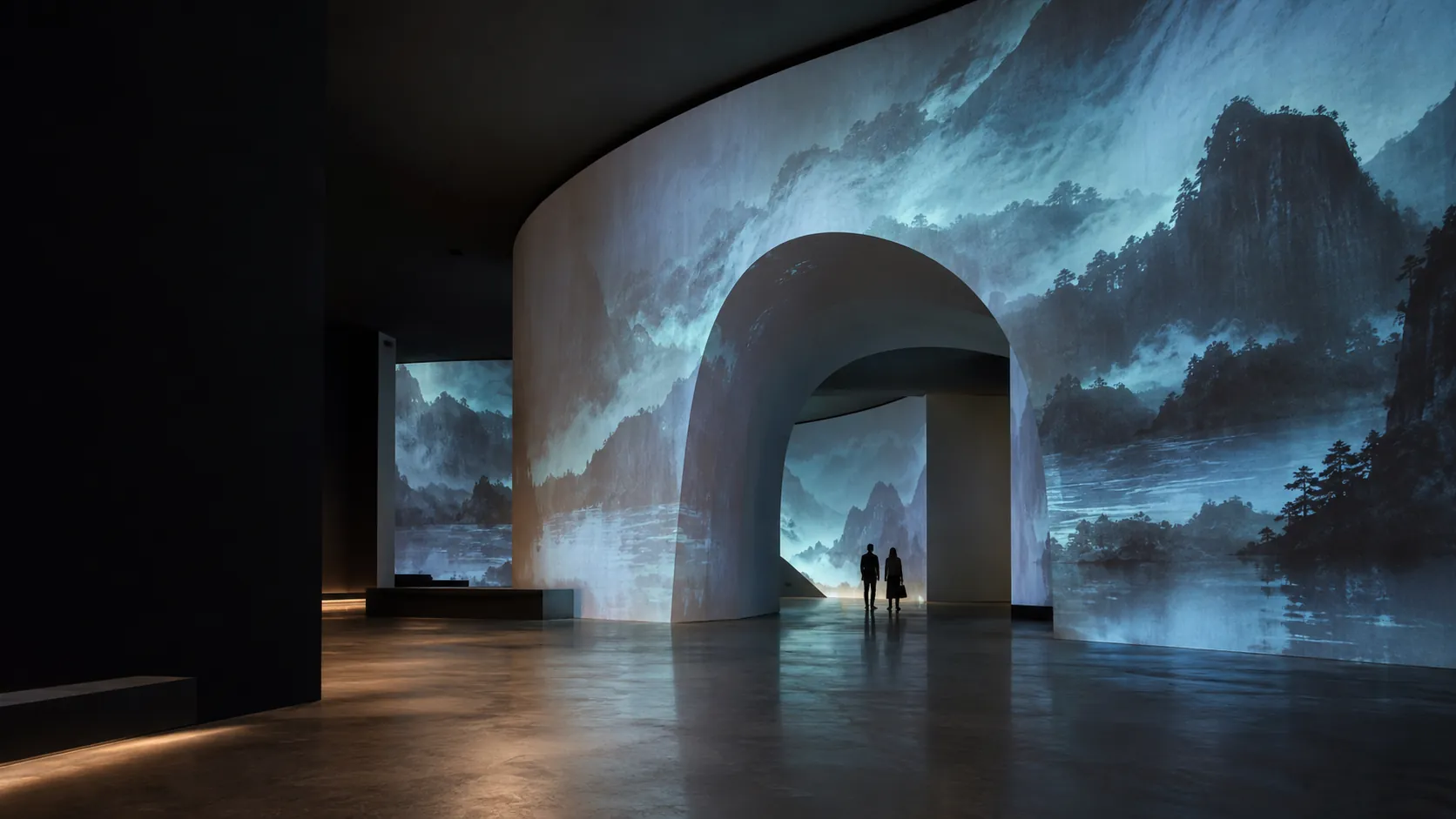 Projected landscape follows a curved museum wall and recessed arch, with two visitors providing scale